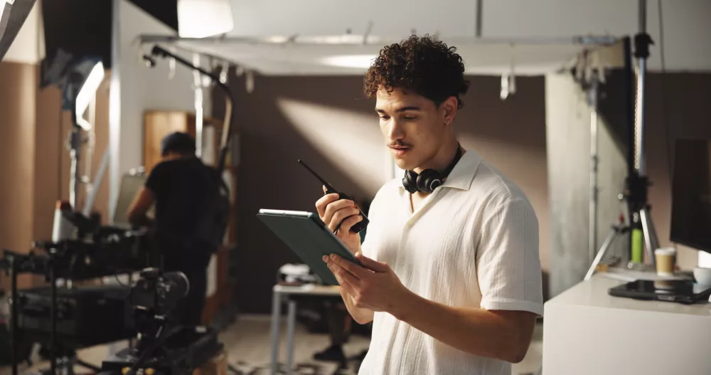 man-filming-radio-with-tablet-set-discussion-reading-script-shooting-schedule-director-backstage-digital-with-crew-advice-scene-tips-performance-guide-movie-production