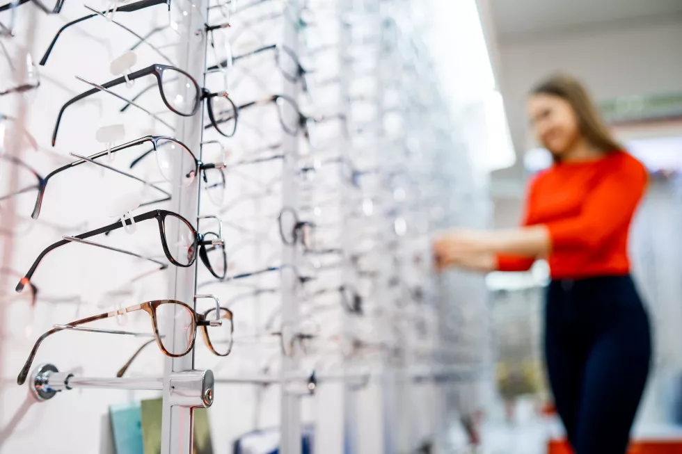 eyeglasses-shop-stand-with-glasses-store-optics-showcase-with-spectacles-modern-ophthalmic-store-closeup-woman-blurred-background