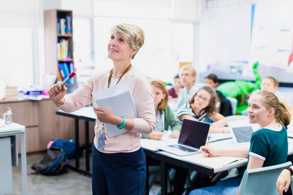 woman-teacher-classroom-holding-marker-teaching-with-attentive-students-woman-teacher-teaching-classroom-with-focused-students-caucasian-woman-teacher-smiling-while-teaching-kids-class