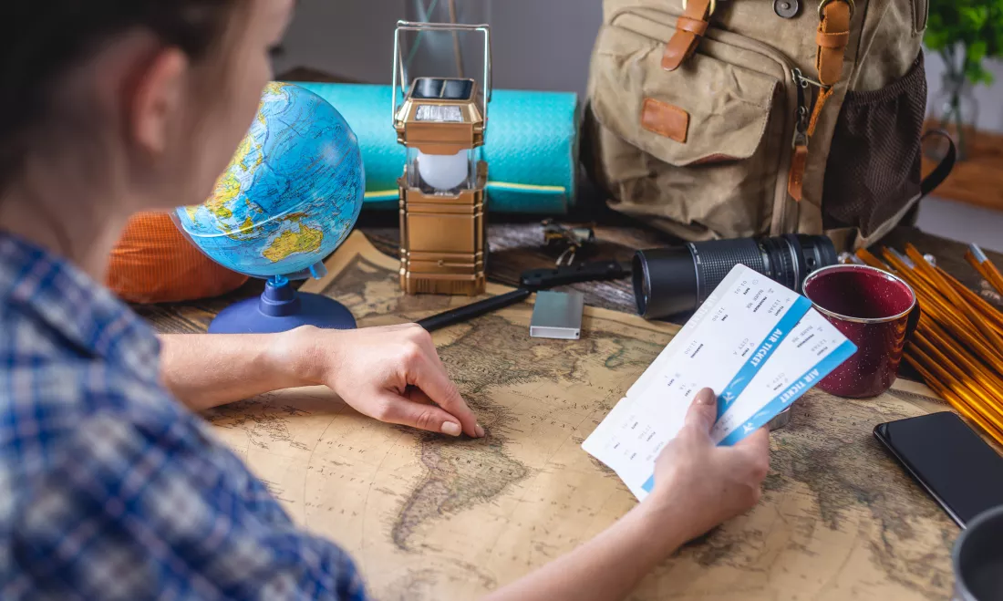 woman-is-choosing-place-her-trip-by-pointing-map-world-wooden-table-with-camping-equipment
