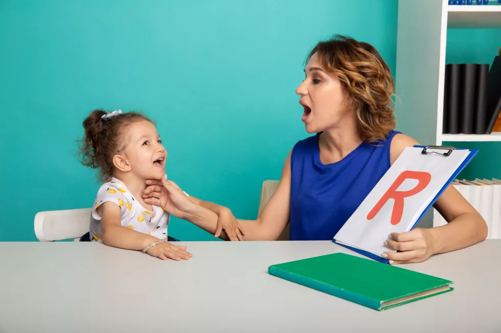 female-therapist-working-with-kid-with-problem-pronunciation-white-cabinet