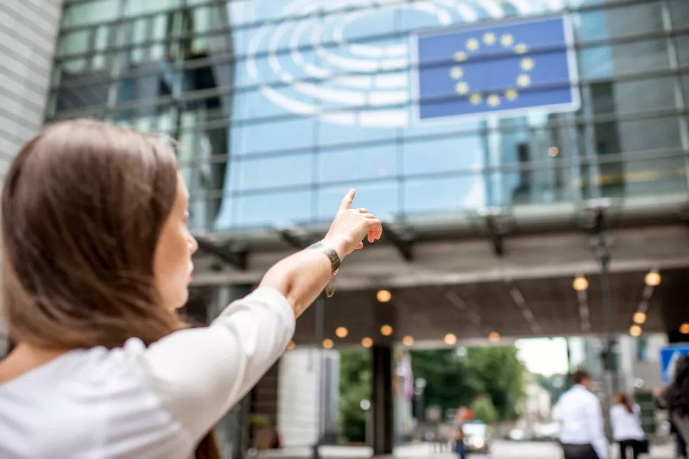 woman-pointing-with-hand-european-flag-parliament-building-brussel(1)