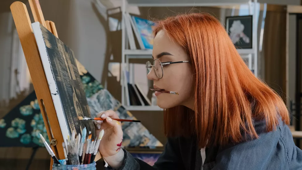 inspired-funny-focused-artist-woman-with-red-hair-girl-painter-wears-glasses-holds-painting-brushes