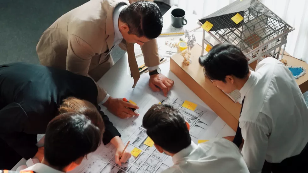 top-view-team-inspect-house-model-while-manager-hold-blueprint-alimentation