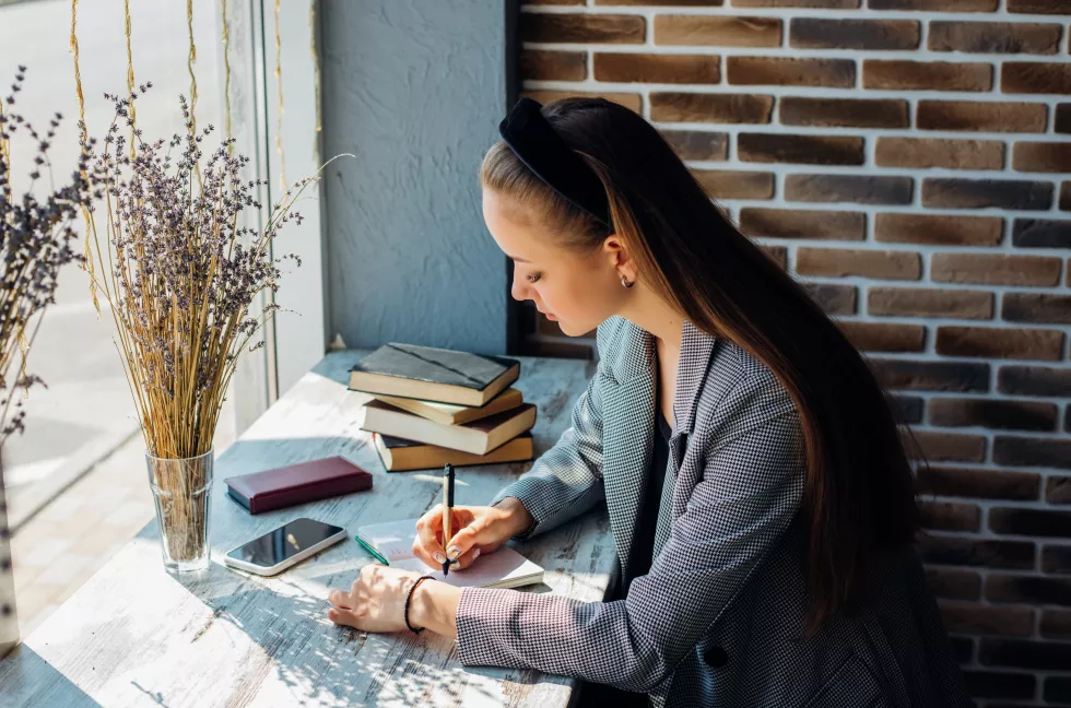 young-woman-is-sitting-table-writing-notebooka-business-woman-works-as-freelancer