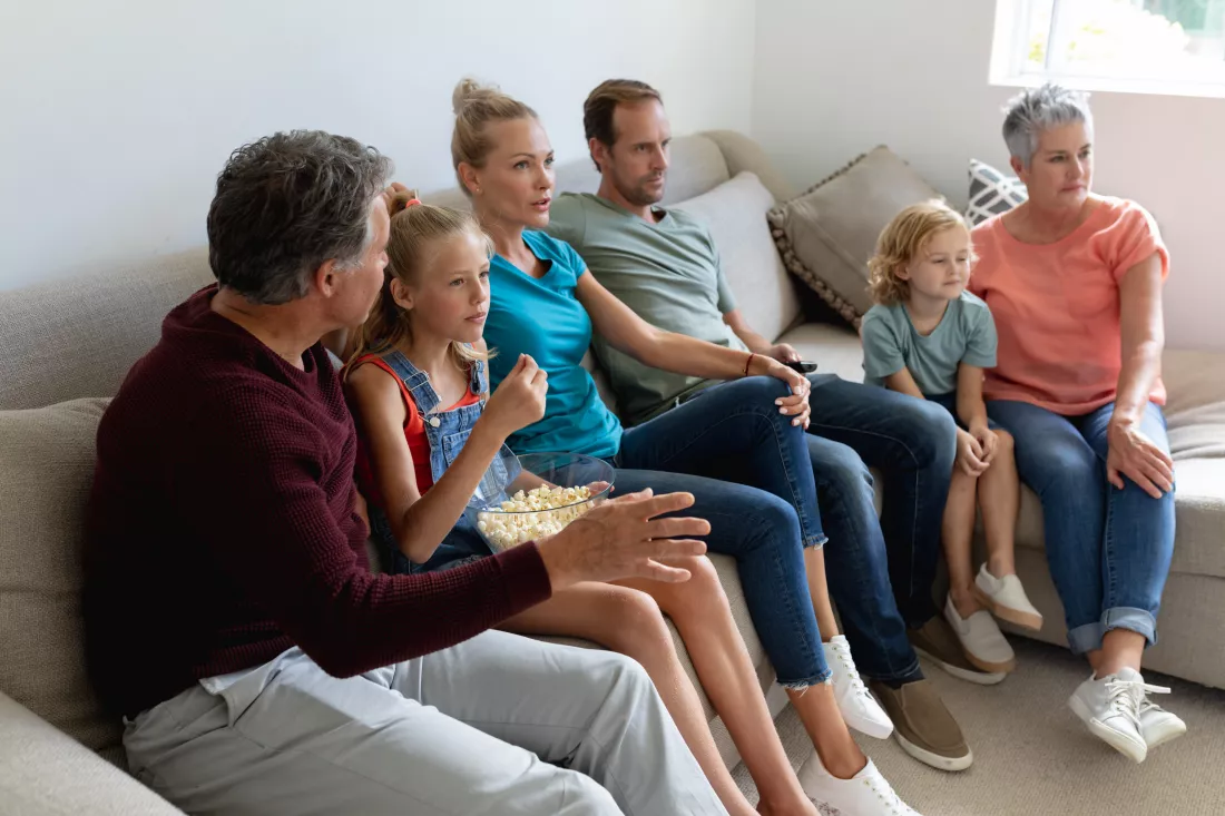 caucasian-parents-grandparents-grandchildren-sitting-couch-watching-tv-eating-popcorn
