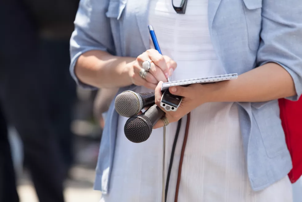 midsection-journalist-holding-microphones-while-writing-note-pad