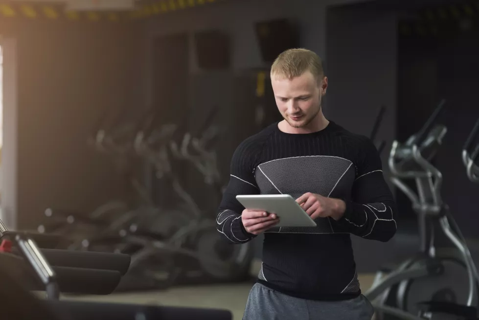athletic-young-man-texting-digital-tablet-before-training-gym-using-application-with-workout-plan-copy-space-bodybuilding-concept