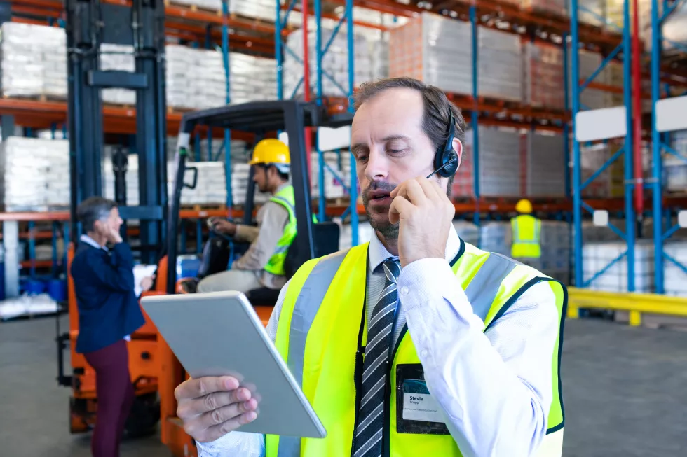 male-supervisor-using-digital-tablet-while-talking-headset-warehouse