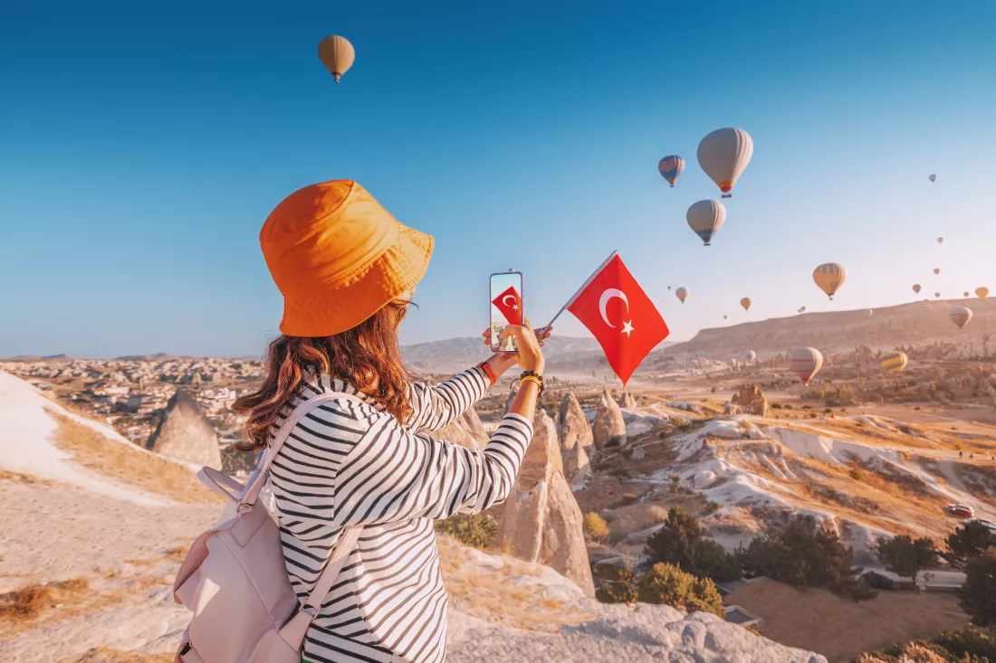 travel-blogger-girl-takes-photos-flying-balloons-cappadocia-turkish-flag-social-media-influencer
