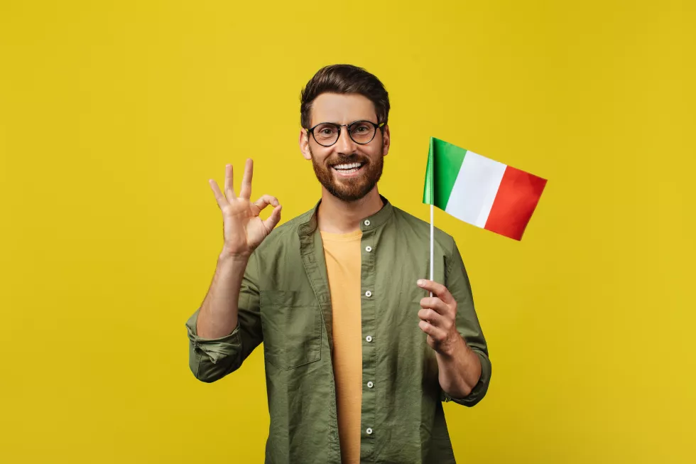 positive-man-showing-flag-italy-gesturing-okey-posing-yellow-studio-background-smiling-camera