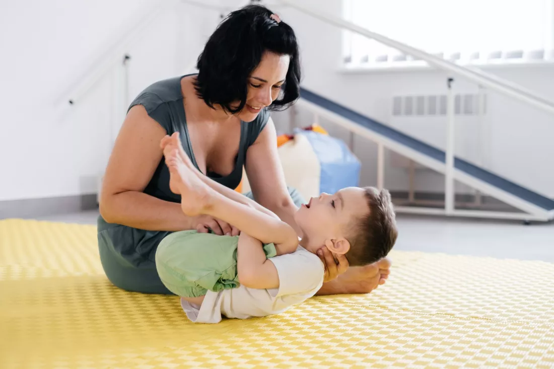 Fizjoterapeutka cwiczy z malym chlopcem na macie w sali rehabilitacji