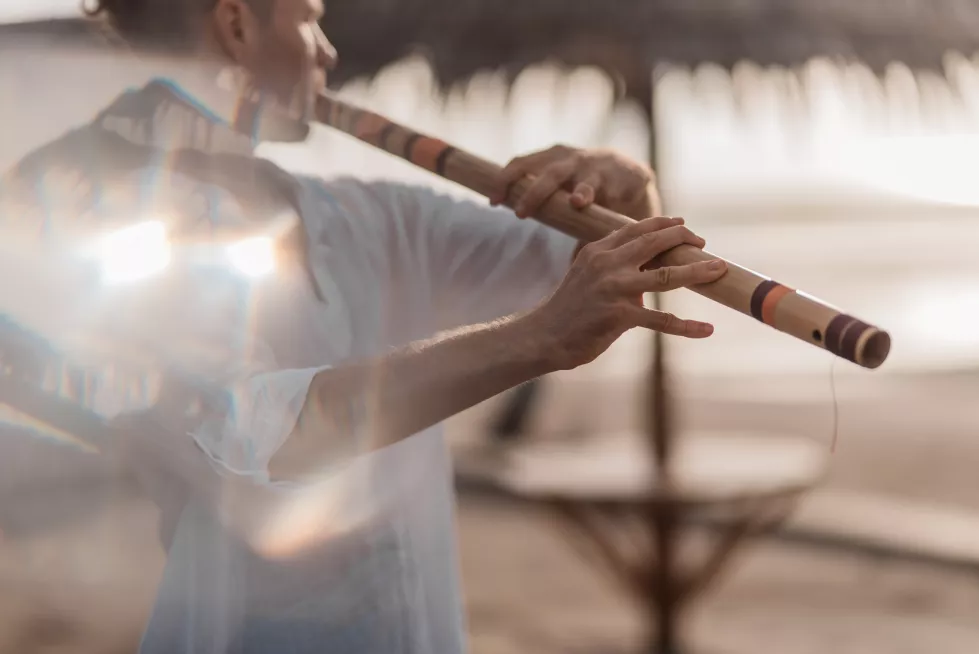 man-playing-wind-instrument-beach-sunrise