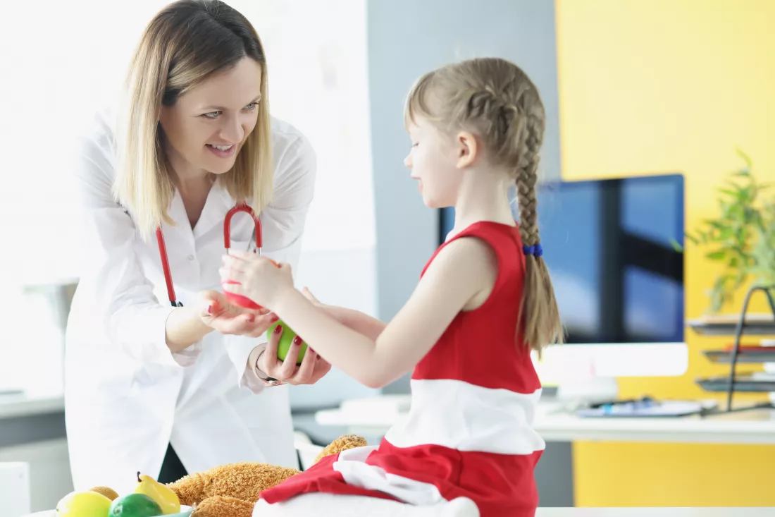 woman-doctor-giving-small-child-apple-clinic