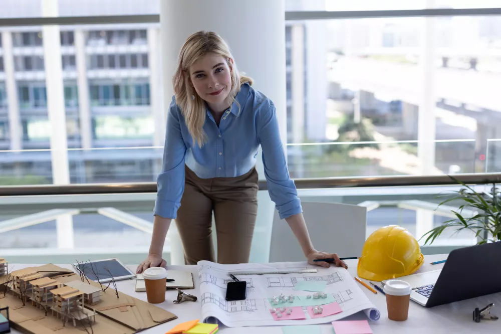 blonde-caucasian-female-architect-looking-camera-desk-office