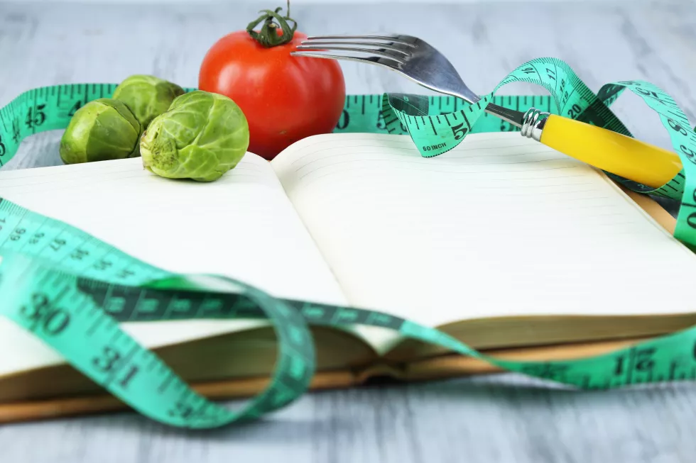 book-with-measuring-tape-vegetables-wooden-background