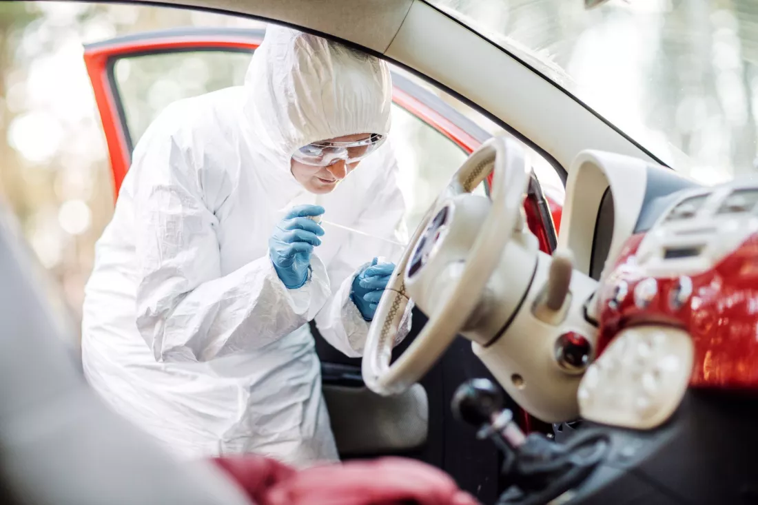 Technik kryminalistyczny w kombinezonie zabezpiecza ślady w samochodzie