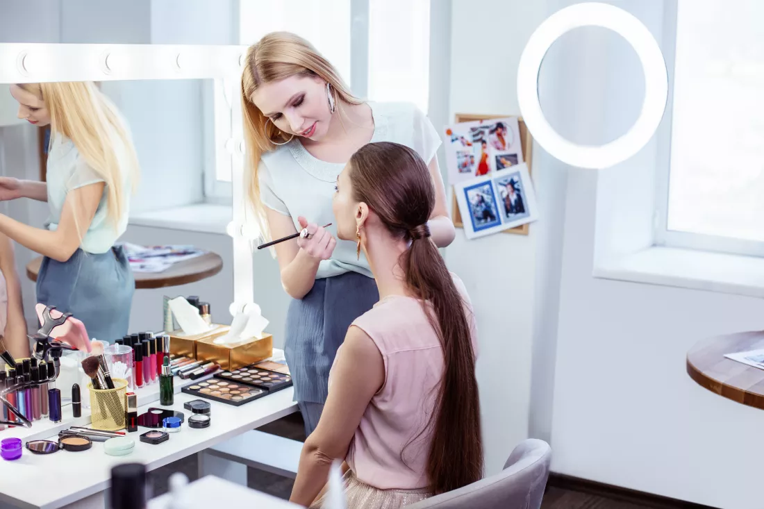 nice-pleasant-woman-standing-near-her-client-while-putting-makeup-her-face