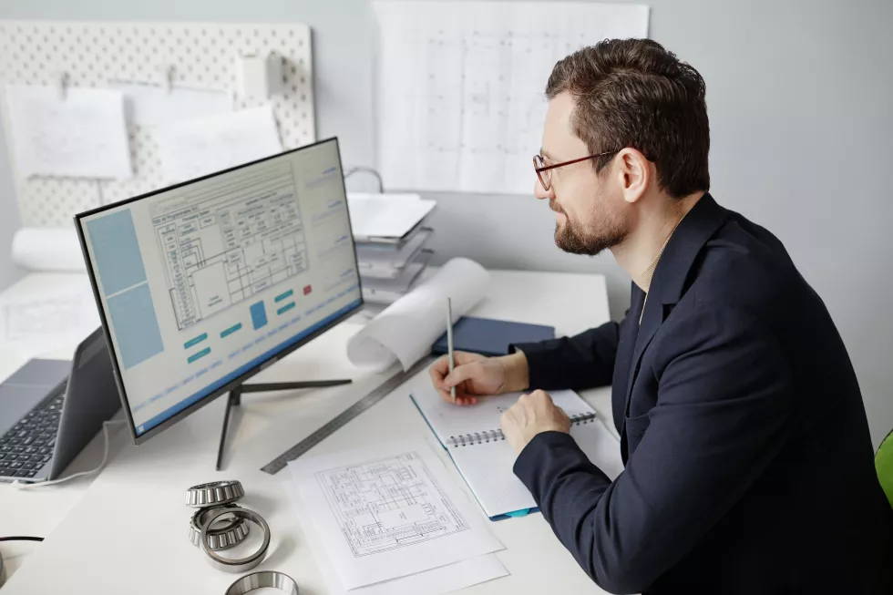 high-angle-portrait-bearded-male-engineer-using-computer-workplace-designing-blueprints-office(1)