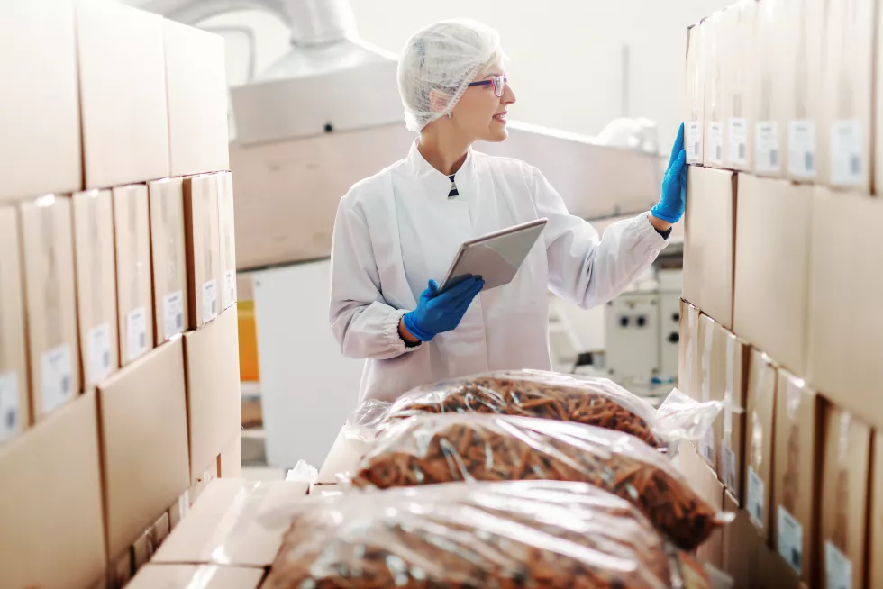 caucasian-blonde-employee-sterile-uniform-standing-dealing-with-logistic-products-food-factory-interior-hand-tablet