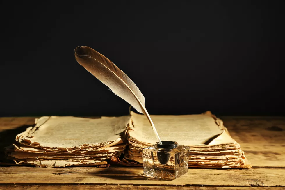 feather-pen-with-inkwell-stack-papers-dark-background