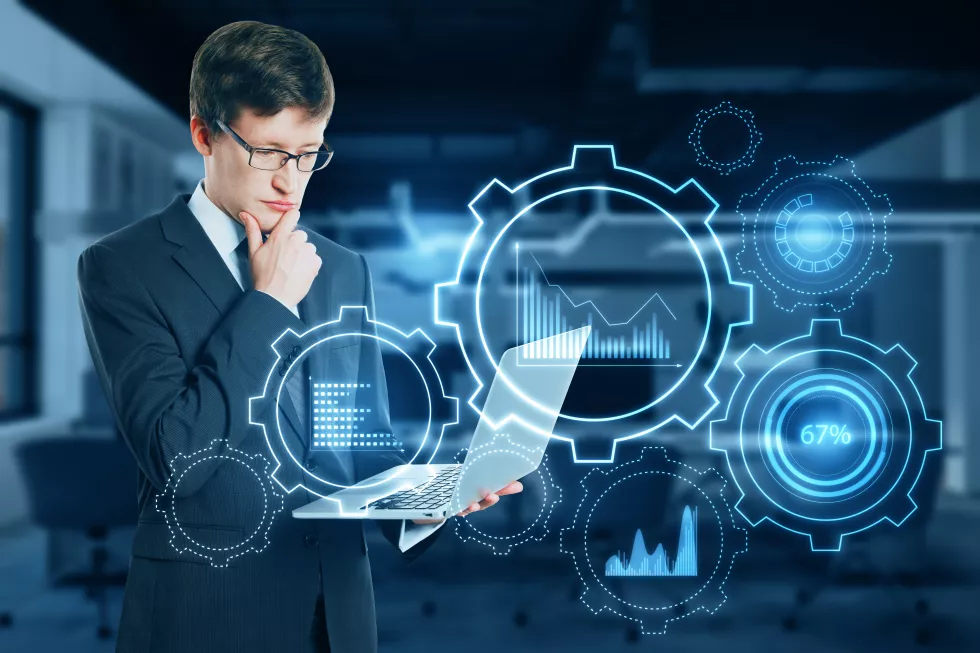 attractive-young-european-businessman-with-laptop-glowing-cogwheel-chart-hologram-blurry-office-interior-background-business-analytics-finance-concept-double-exposure