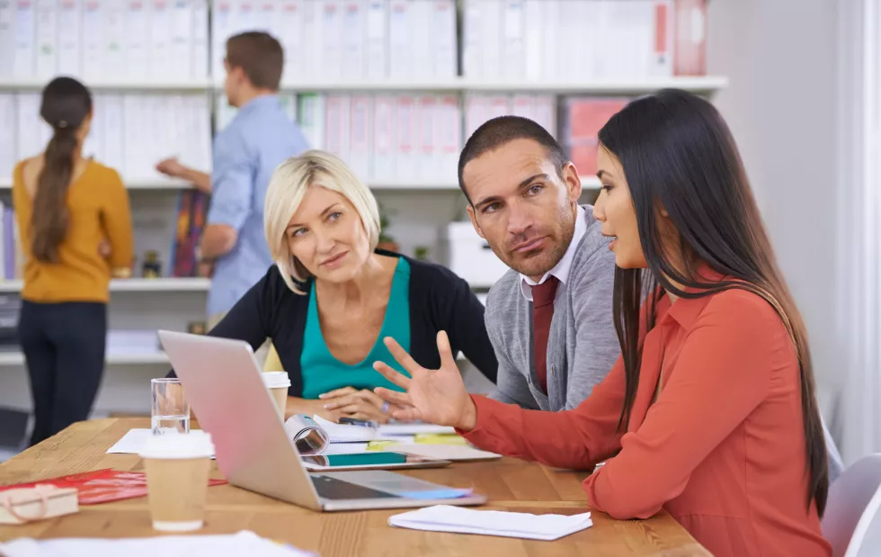 we-have-come-up-with-solution-three-coworkers-brainstorming-around-laptop-while-their-colleagues-read-files-background