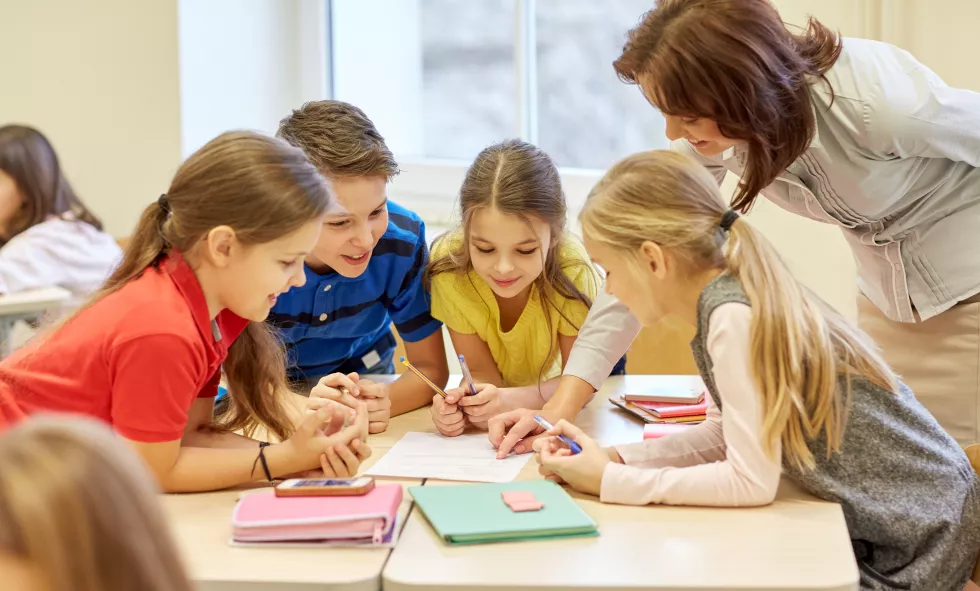 education-elementary-school-learning-people-concept-teacher-helping-school-kids-writing-test-classroom