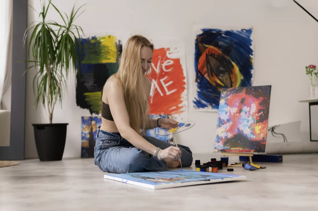 An art student paints a large canvas in a bright studio.