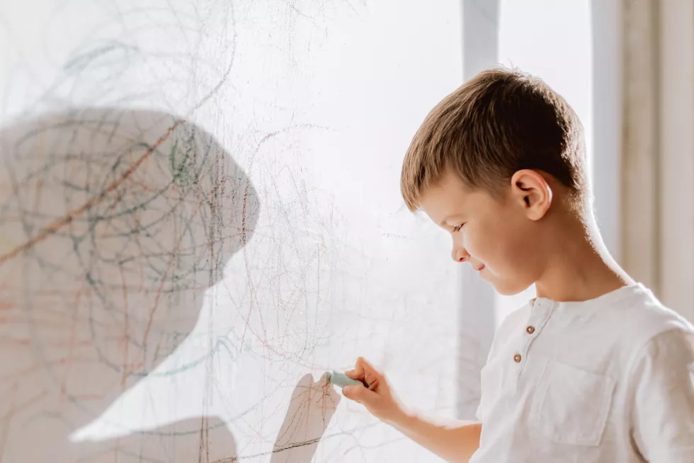 cheerful-boy-with-pencil-stands-near-wall-that-he-painted-child-is-engaged-creativity-home