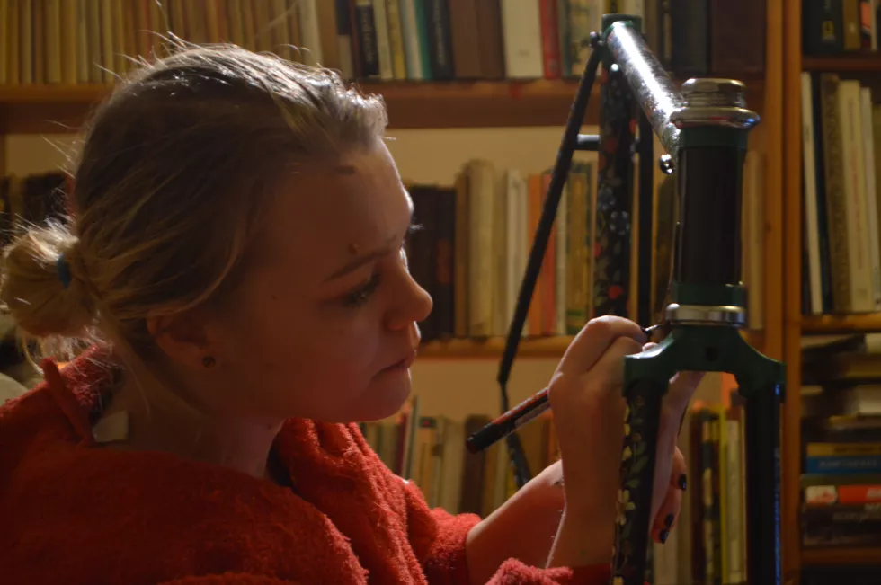 woman-painting-bicycle-frame-against-bookshelf