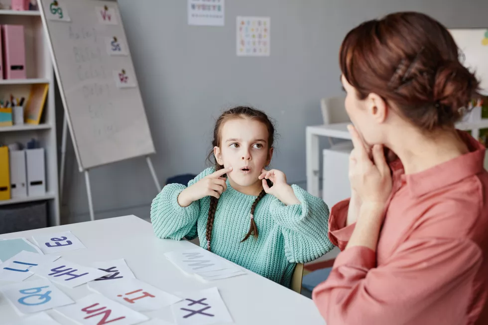 little-schoolgirl-learning-read-english-words-together-with-teacher-while-they-studying-desk-classroom