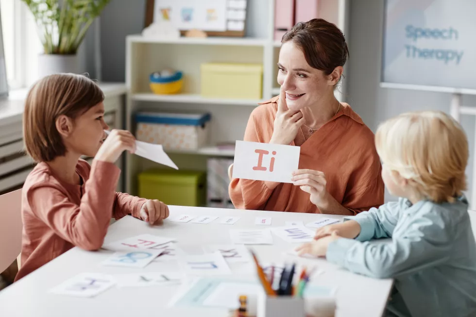 young-woman-sitting-table-with-children-showing-card-with-letter-teaching-them-read