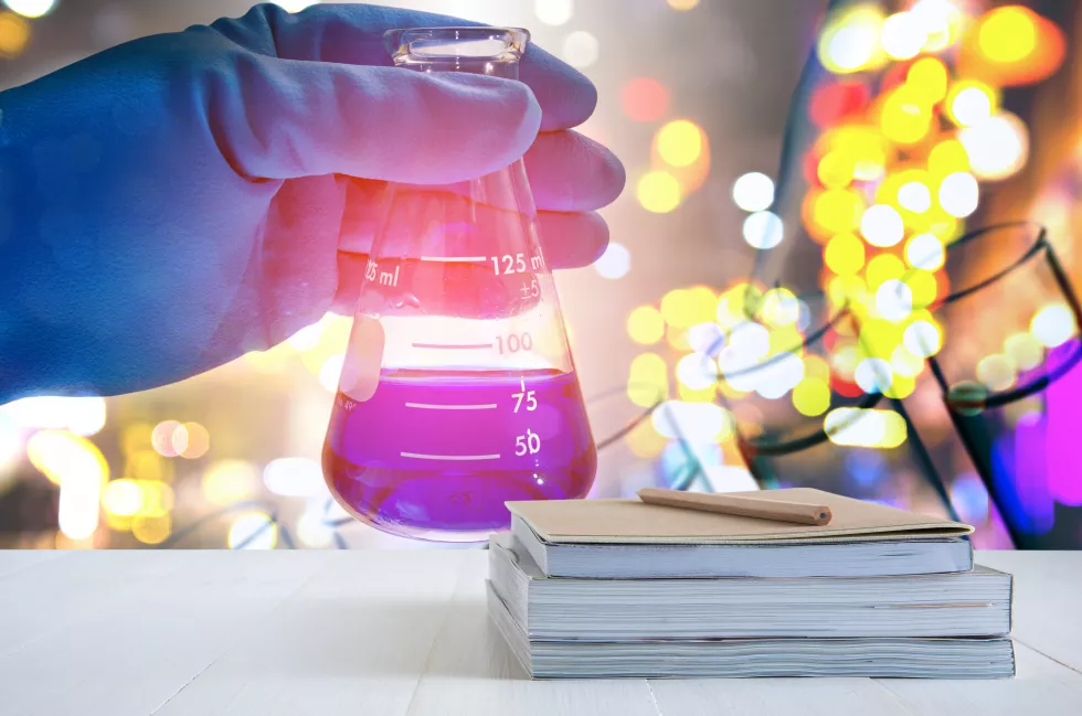 cropped-hand-scientist-holding-chemical-flask-against-illuminated-lights
