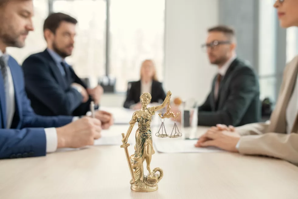 focus-golden-themis-with-scales-justice-sward-placed-lawyers-table-colleagues-sitting-across-from-each-other-background