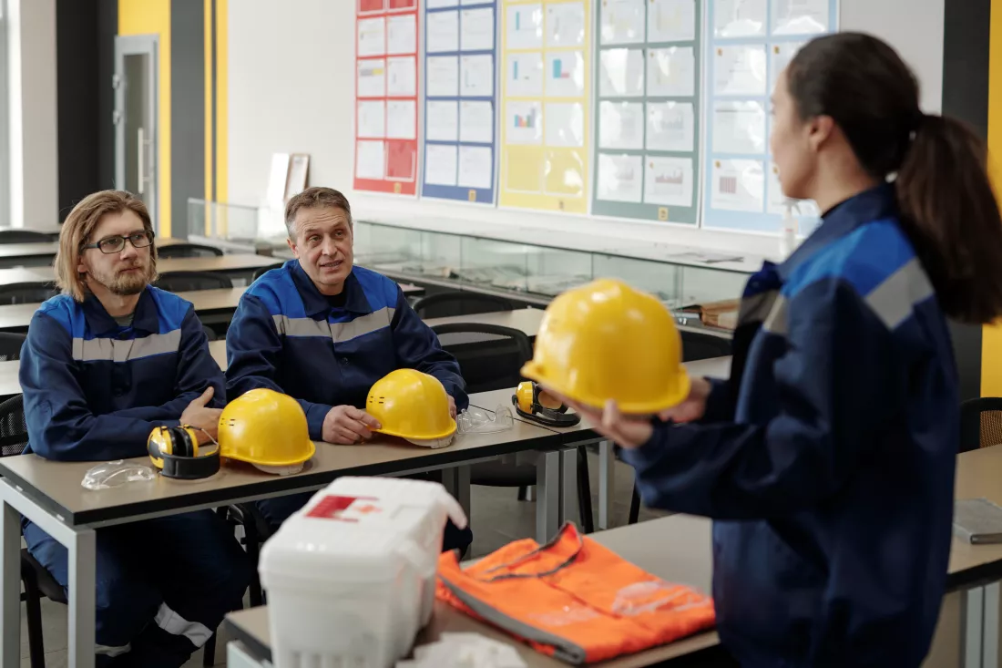 female-instructor-holding-hardhat-explaining-occupational-safety-rules-workers-sitting-table