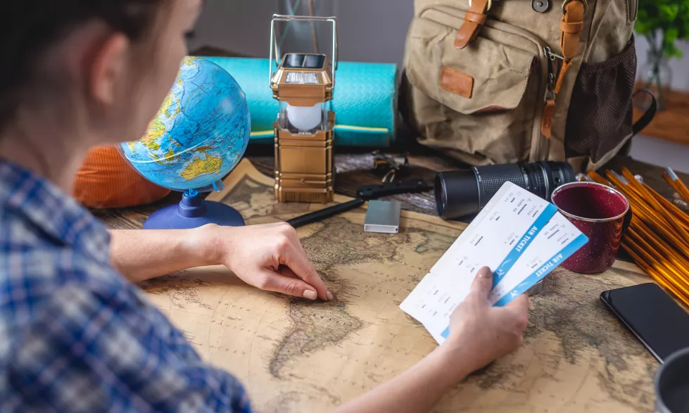 woman-is-choosing-place-her-trip-by-pointing-map-world-wooden-table-with-camping-equipment