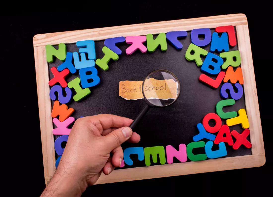 copped-hand-holding-magnifying-glass-colorful-alphabets-writing-slate