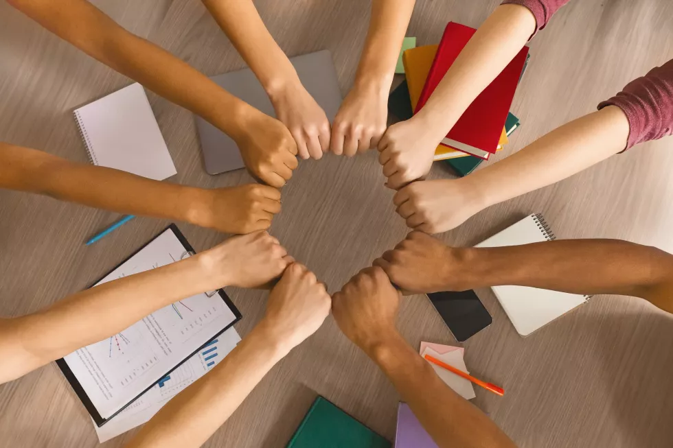 multiracial-students-joining-hands-together-preparing-common-academic-project-top-view